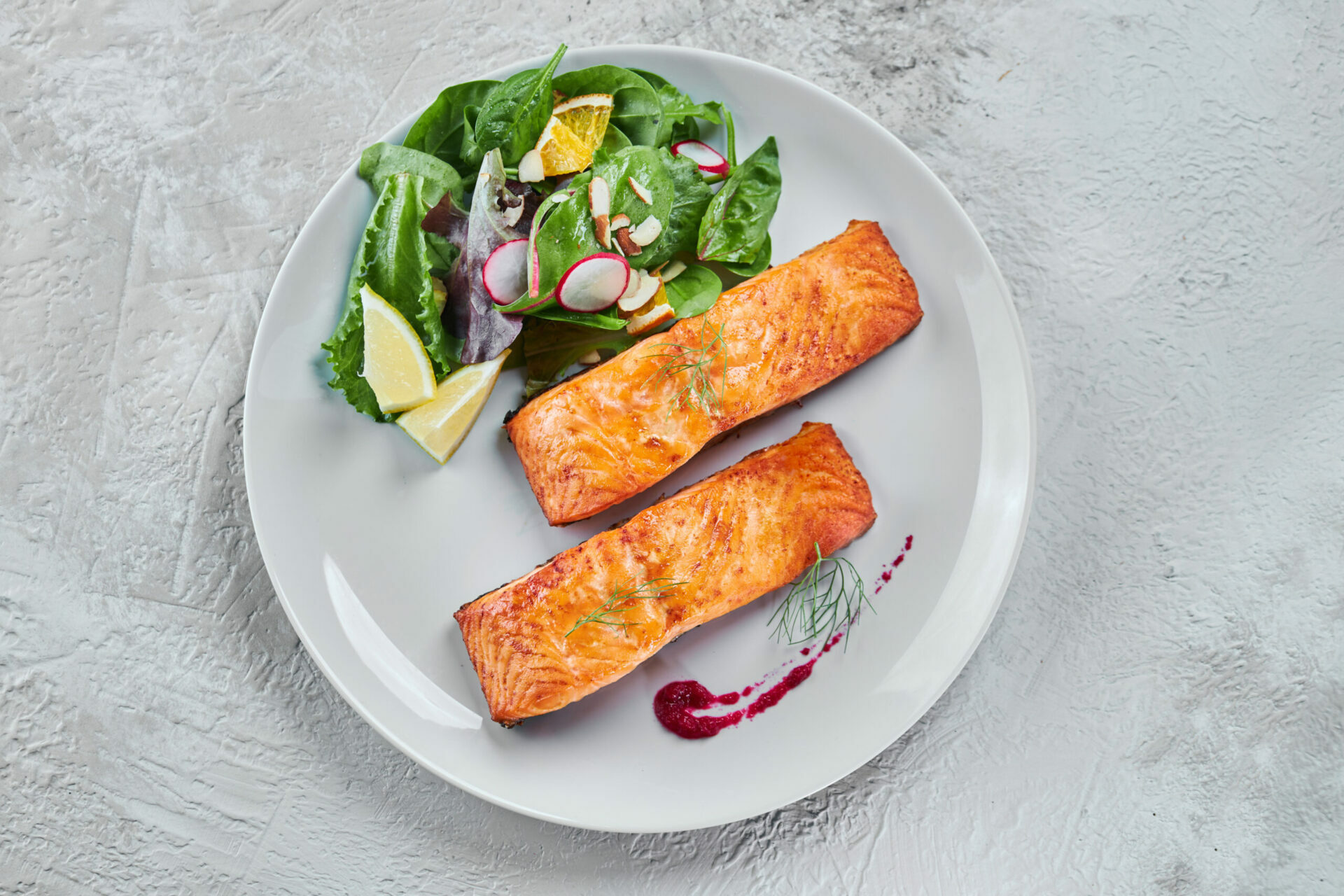 Salmone cotto con insalata, limone e una salsa rossa.