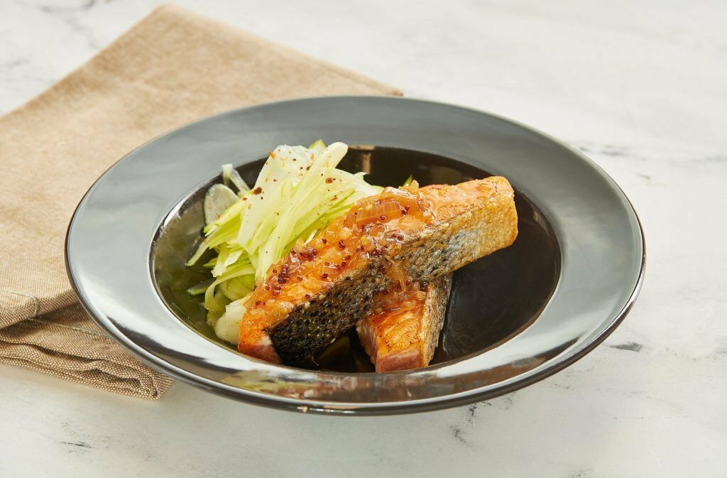 Salmone scottato con julienne di verdure su un piatto scuro con tovagliolo.