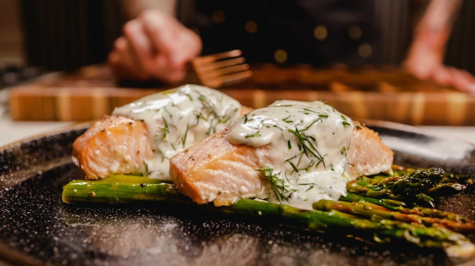 Salmone con salsa cremosa e asparagi su piatto scuro.
