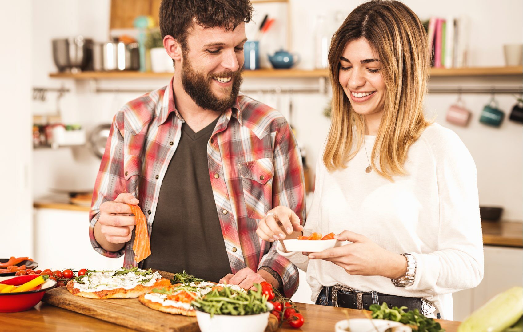 Coppia felice prepara pizze gourmet in cucina, aggiungendo ingredienti freschi.