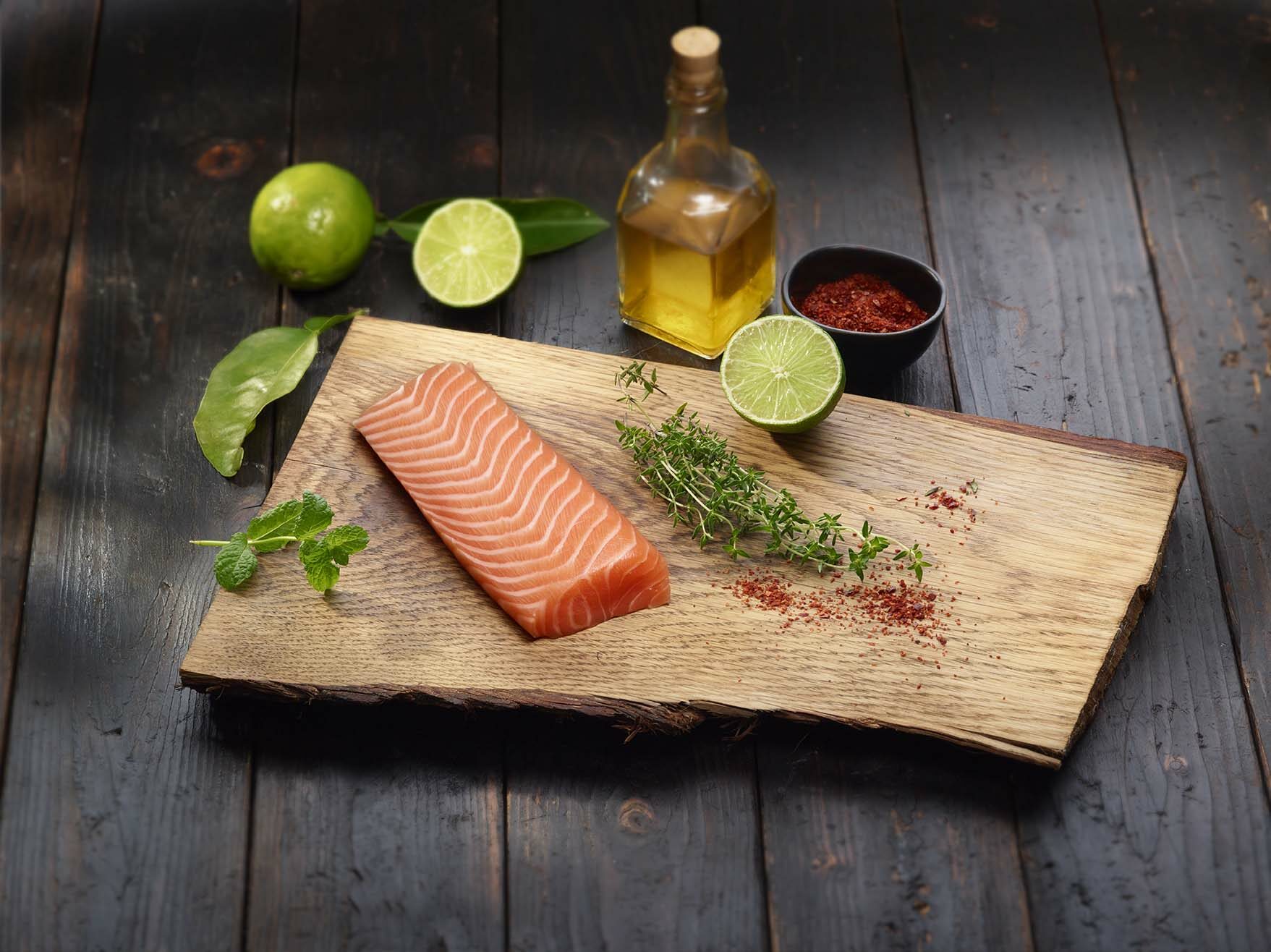 Filetto di salmone crudo con lime, timo, menta, olio e spezie su tagliere rustico.