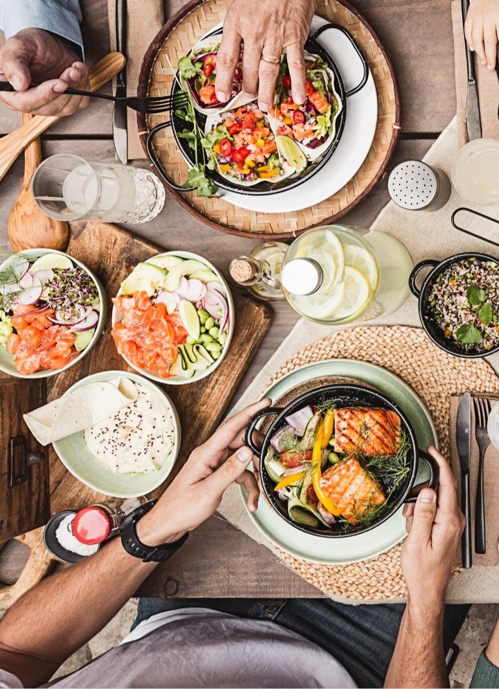 Tavola estiva con salmone grigliato, poke bowl, tacos e insalate fresche.