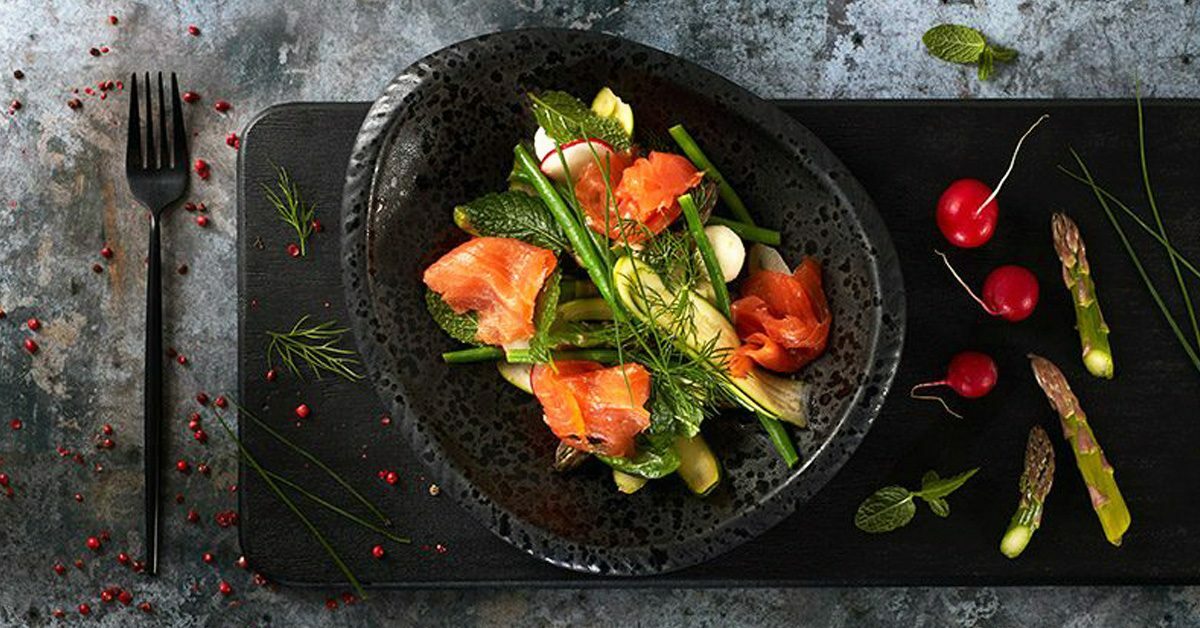 Insalata con salmone affumicato, asparagi, ravanelli e aneto su piatto nero.