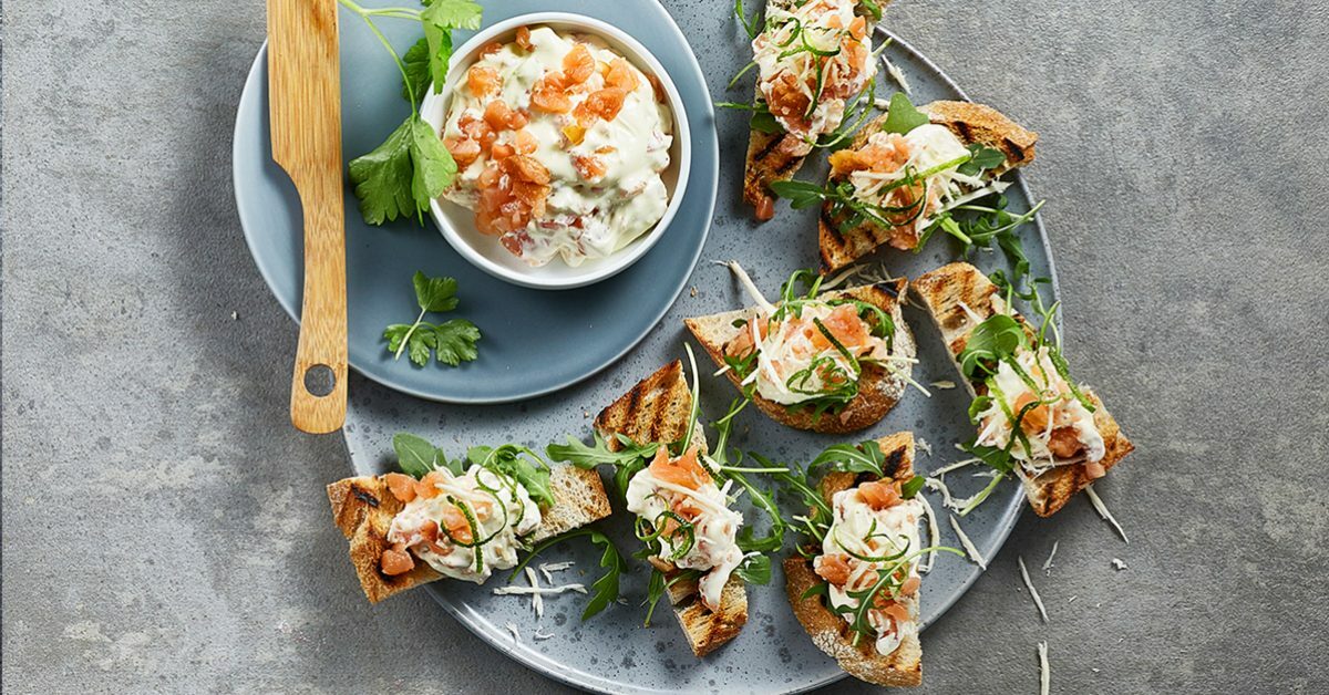 Bruschette con salmone, crema e rucola servite su un piatto grigio.