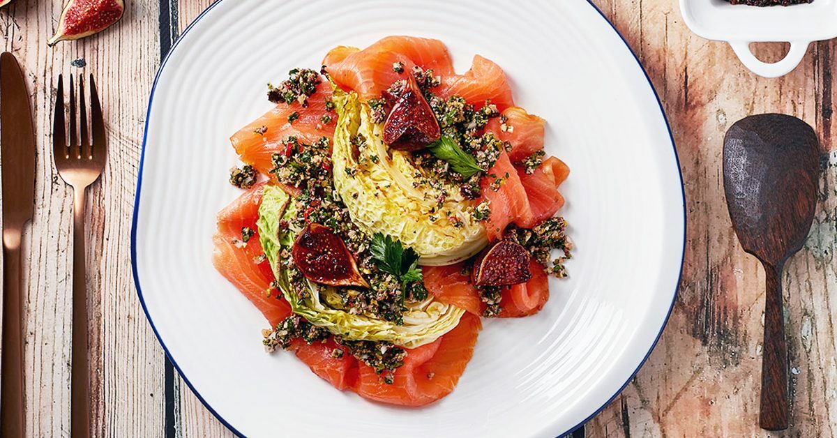 Salmone affumicato con cavolo brasato, fichi e salsa croccante su piatto bianco.