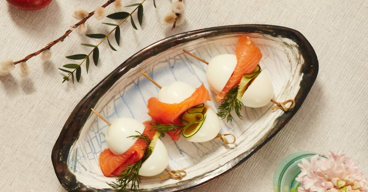 Uova sode con salmone e cetriolo su stuzzicadenti, servite su piatto ovale.