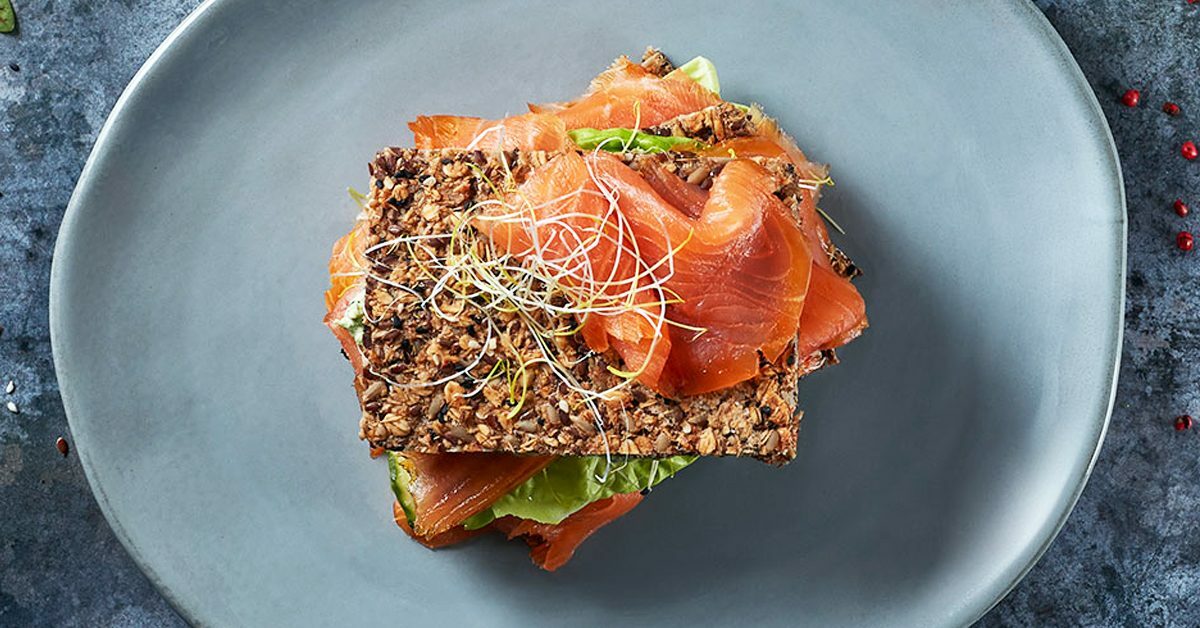 Tramezzino di pane integrale con salmone affumicato, germogli e lattuga.
