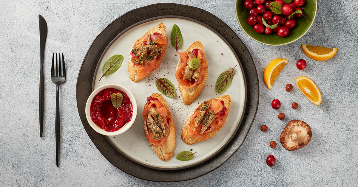 Bruschette con salmone affumicato, salsa di mirtilli rossi e guarnizioni festive.