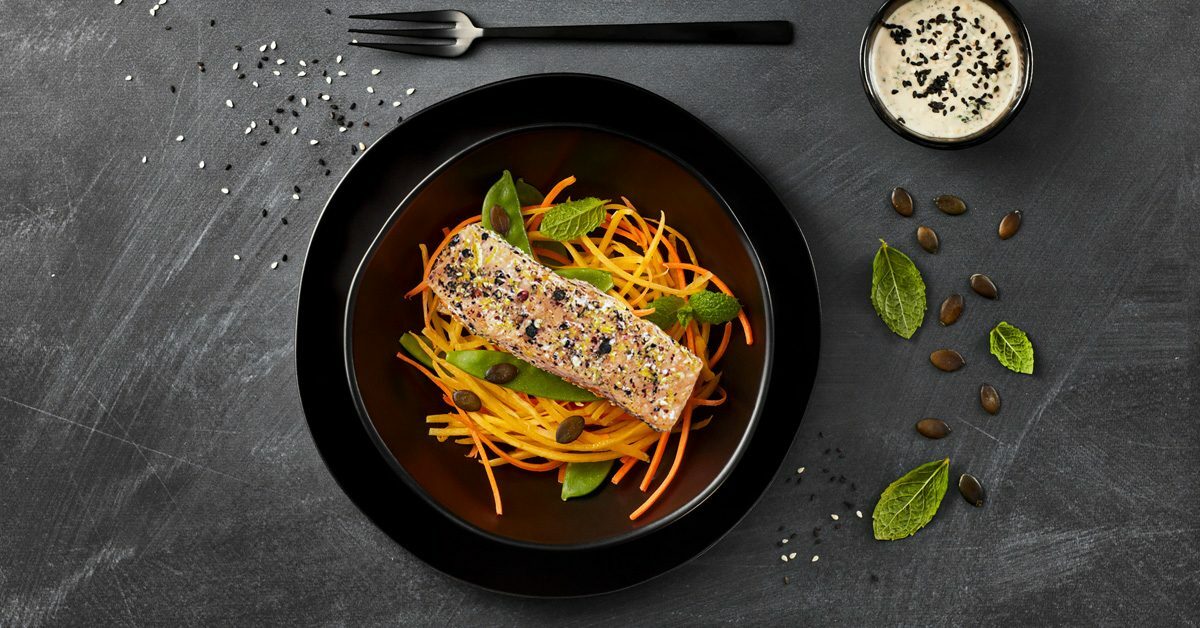 Salmone al pepe su letto di carote julienne, guarnito con semi e menta.