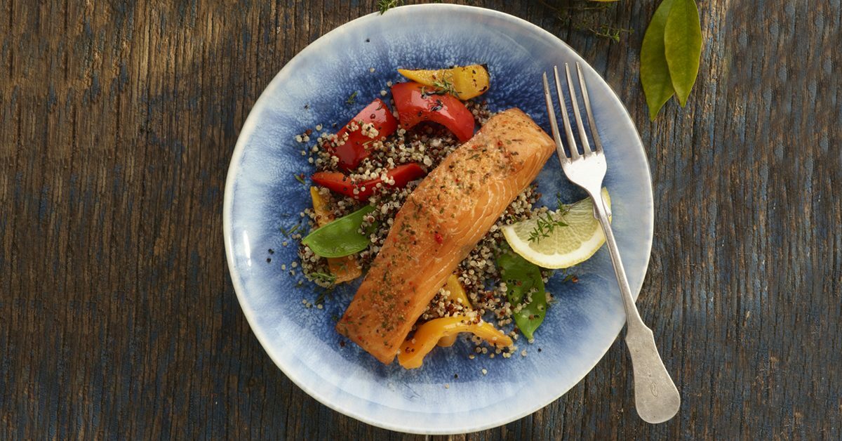 Salmone con quinoa, peperoni e limone su piatto blu.