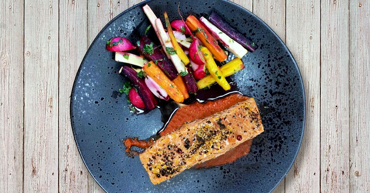Salmone con carote miste e ravanelli su piatto scuro.