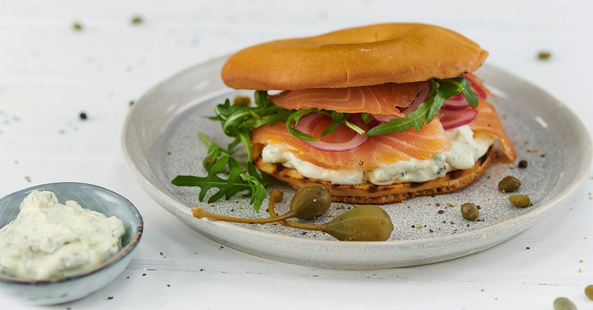 Bagel con salmone affumicato, rucola, cipolla rossa e crema al formaggio su piatto.