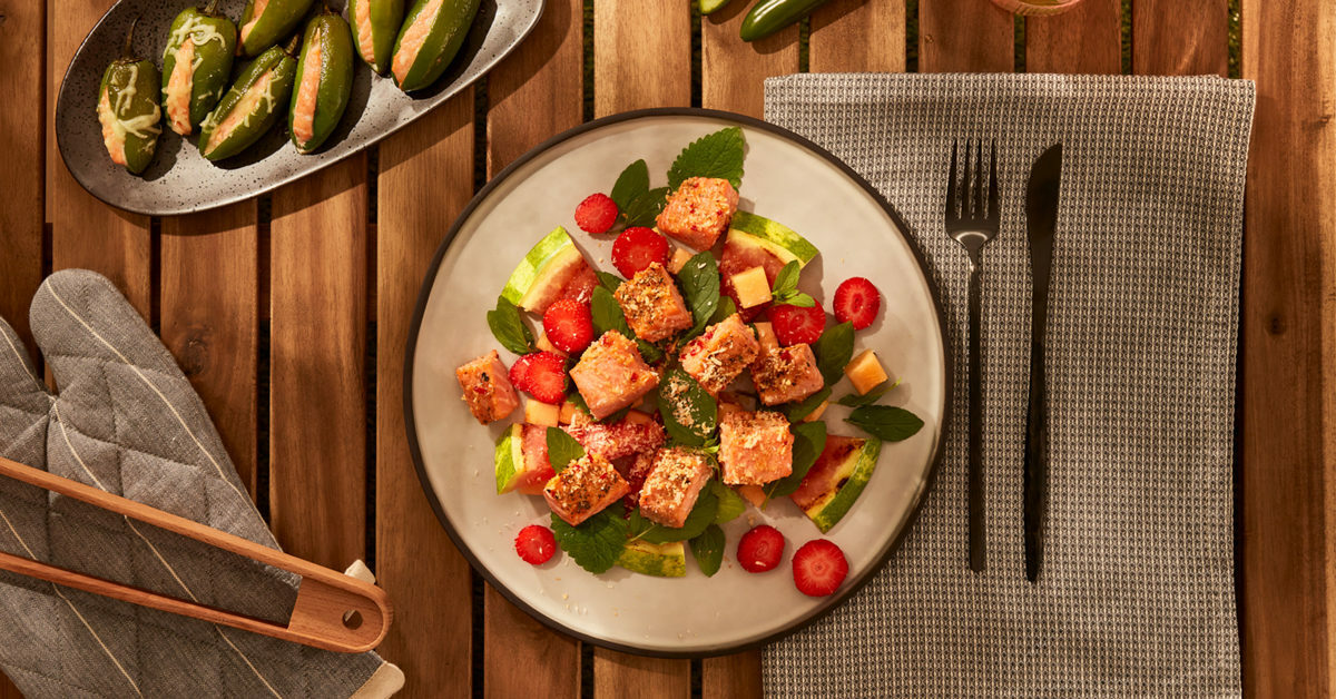 Insalata di salmone con anguria, fragole e melone, guarnita con menta.