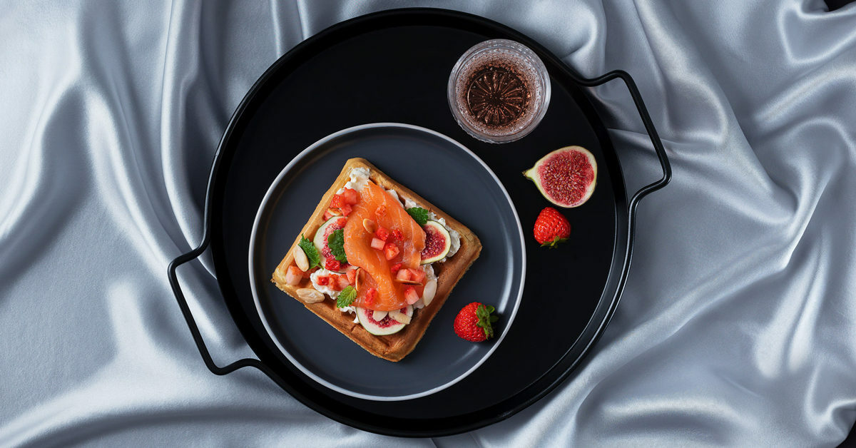 Waffle con salmone, fichi, fragole e panna su vassoio con seta.