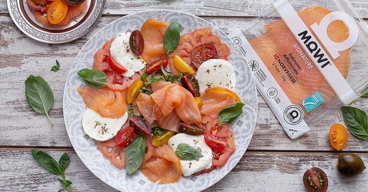 Insalata di salmone affumicato, mozzarella, pomodorini e basilico su un piatto decorato.