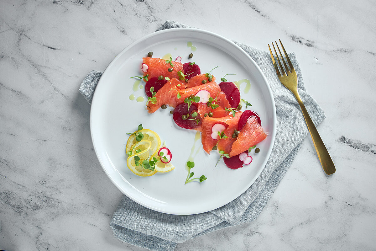 Salmone affumicato con barbabietola, limone e erbe fresche su piatto bianco.