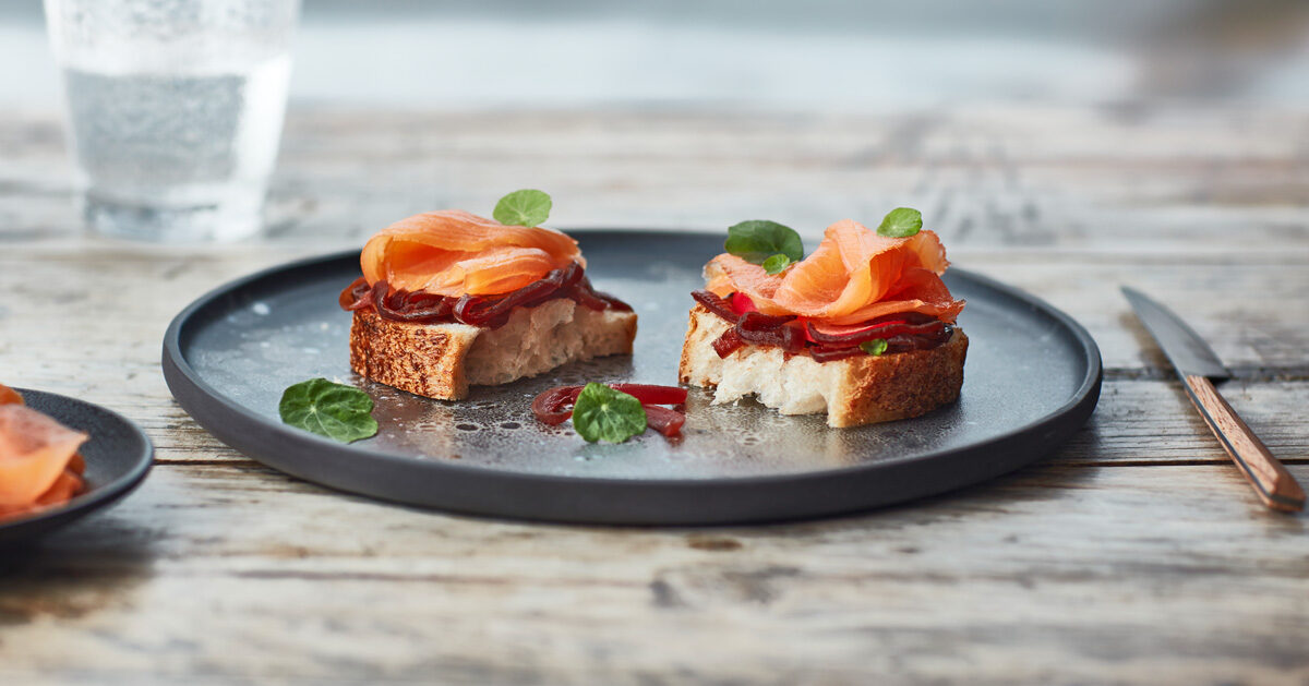 Bruschette con salmone, barbabietola e foglioline verdi su piatto scuro.