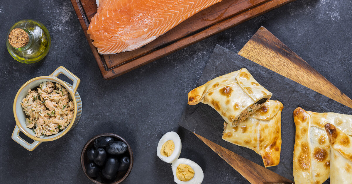 Empanadas di salmone con contorni: salmone crudo, insalata di salmone, olive nere, uova sode e olio.