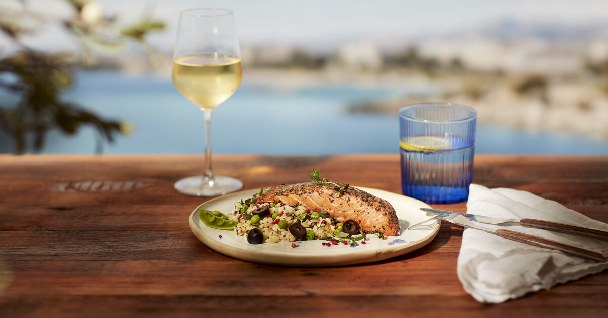 Salmone con riso e olive, vino bianco, acqua al limone su un tavolo di legno vista mare.