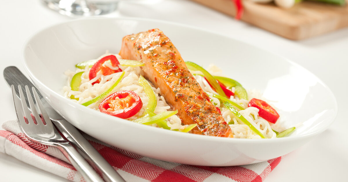 Salmone al forno con riso, peperoni e pomodoro su una ciotola bianca.