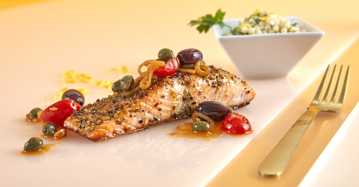 Salmone al pepe nero con olive, capperi e pomodorini, contornato da cuscus.