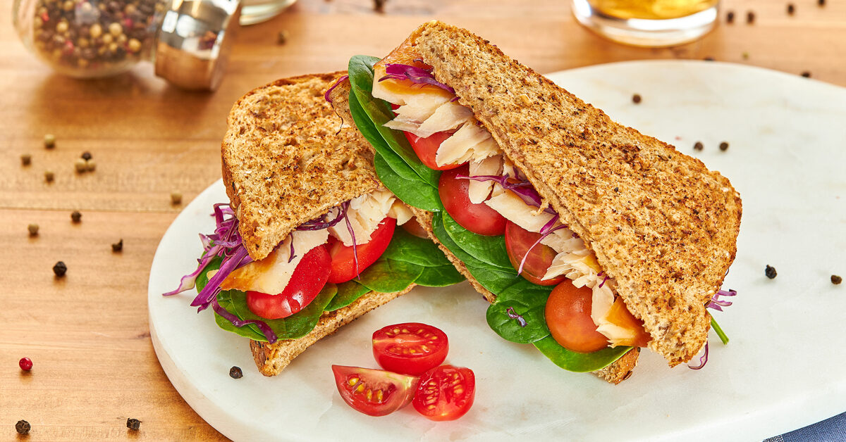 Sandwich di pane integrale con pesce, spinaci, pomodoro e cavolo rosso.