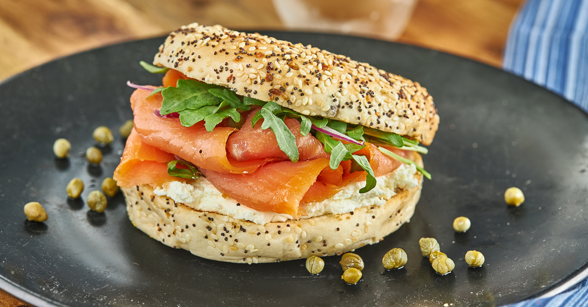 Bagel con salmone affumicato, formaggio cremoso, rucola e capperi.