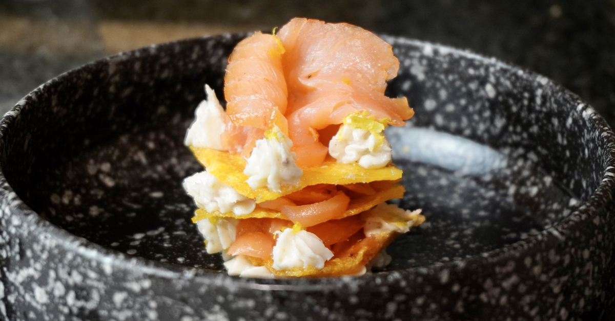 Croccante salmone, crema e zest di limone impilati in una ciotola nera.
