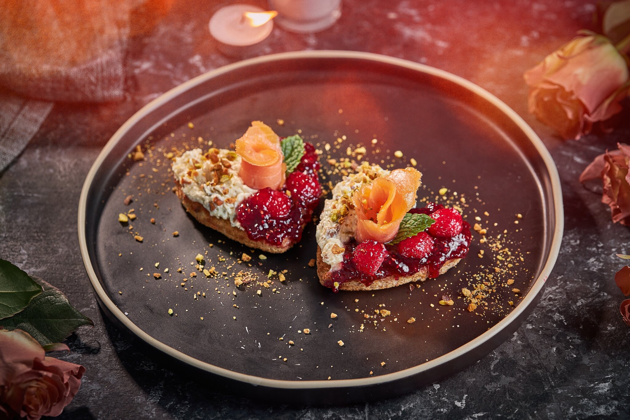 Due tartine a forma di cuore con salmone affumicato, frutti di bosco e pistacchi.