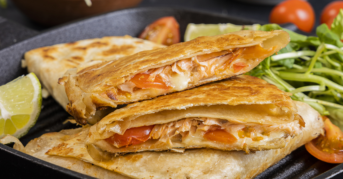 Quesadilla di salmone e pomodoro con contorno di insalata e lime su bistecchiera.