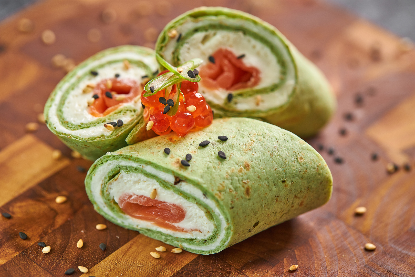 Rotolini di crepe verdi con salmone, formaggio e uova di salmone.