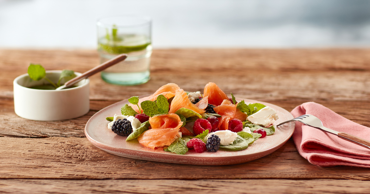 Insalata con salmone affumicato, frutti di bosco e formaggio su piatto rosa.