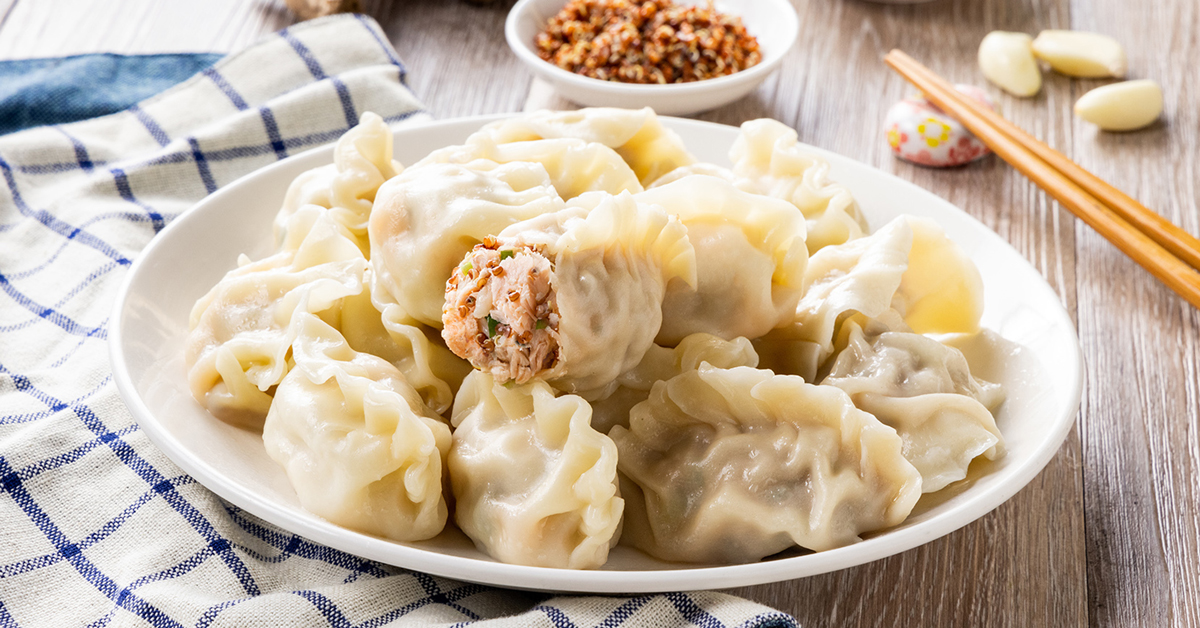 Piatto di ravioli al vapore ripieni di carne e verdure, con bacchette sullo sfondo.