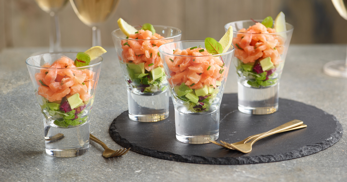 Tartare di salmone e avocado in bicchierini, guarniti con limone.