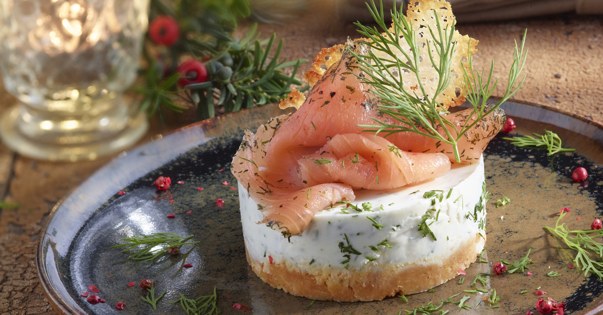 Salmone affumicato su tortino bianco con aneto e decorazioni festive su piatto scuro.