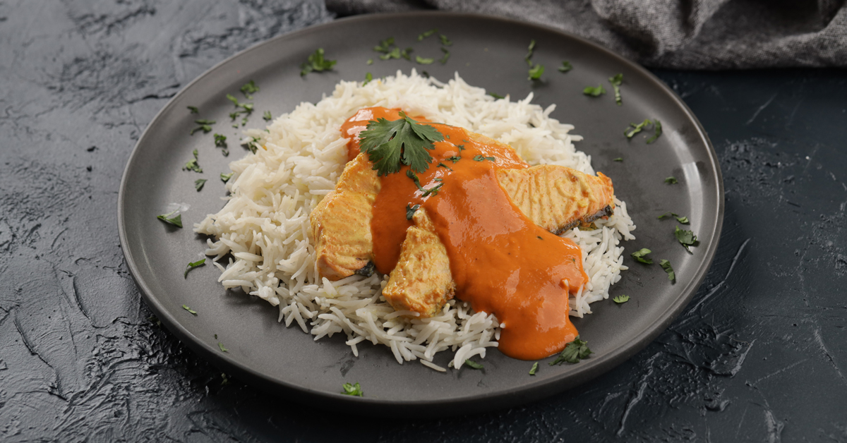 Piatto di riso basmati con salmone in salsa cremosa arancione, guarnito con coriandolo fresco.